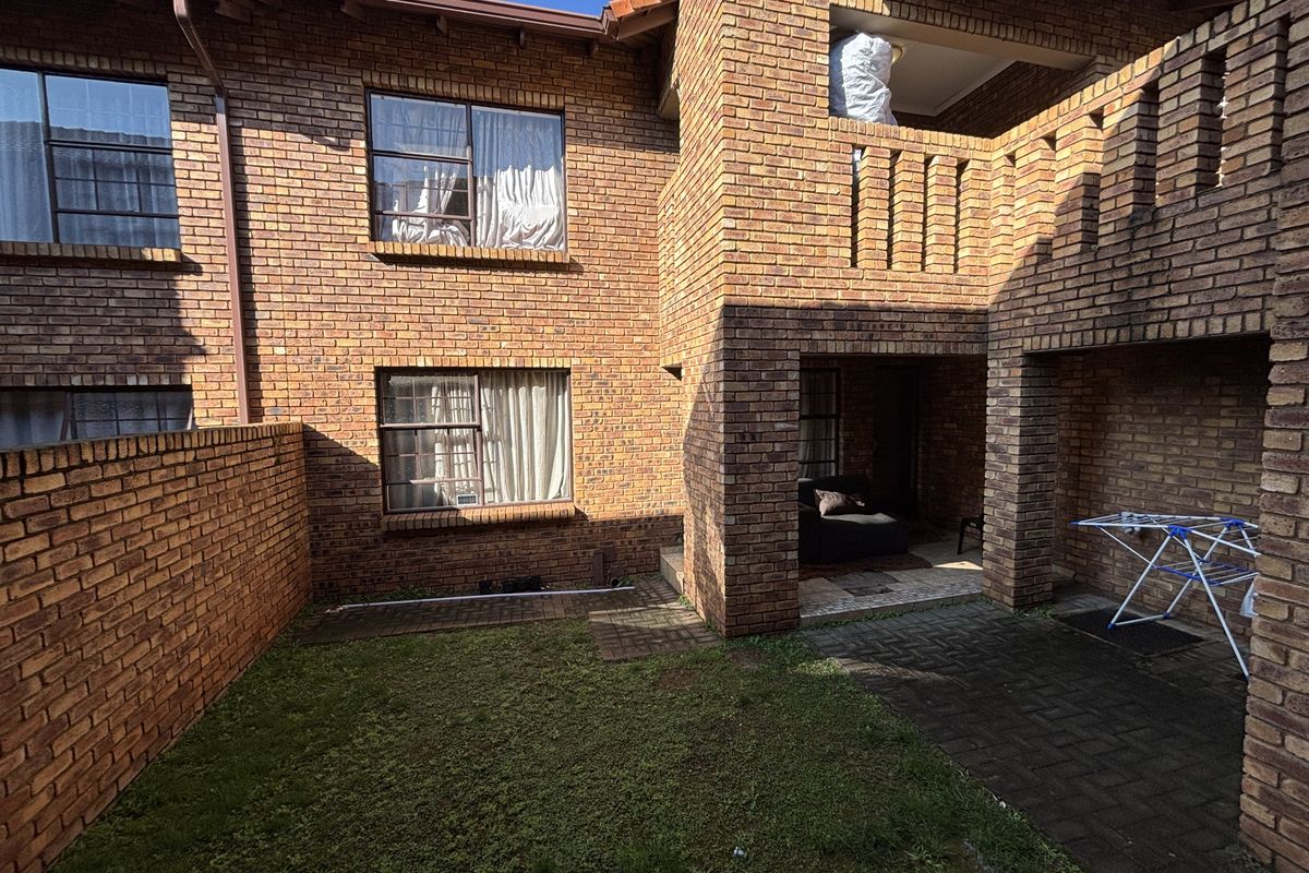 Rear view of a face brick townhouse featuring a paved patio area, a small lawn, and an upper-level balcony.