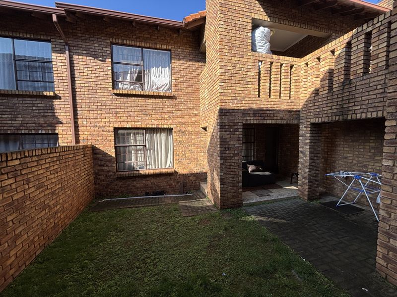 Rear view of a face brick townhouse featuring a paved patio area, a small lawn, and an upper-level balcony.