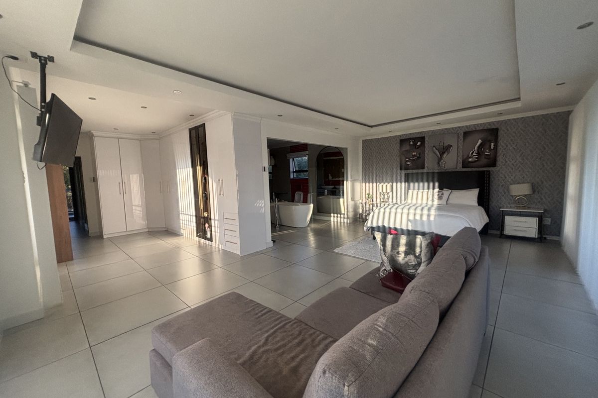 Spacious open-plan bedroom featuring a recessed ceiling, built-in cabinetry, tiled flooring, and an integrated en-suite bathroom area.