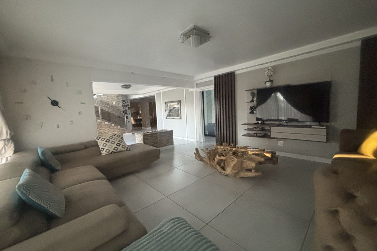 Spacious living room featuring large format floor tiles, modern recessed ceiling lighting, and a custom built-in media console with decorative wall accents.