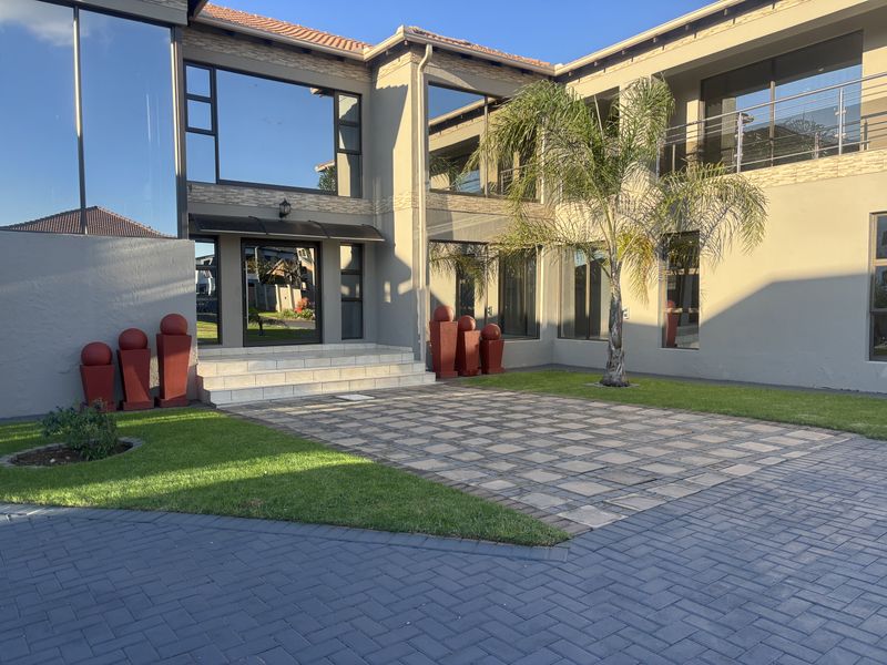 Modern double-story residence featuring a paved driveway, landscaped garden, large glass windows, and a balcony with stainless steel railings.