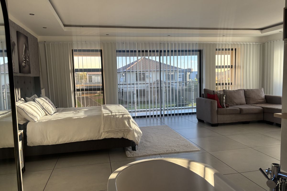 Spacious bedroom featuring large format floor tiles, recessed ceiling lighting, and sliding glass doors leading to a balcony, with an integrated freestanding bathtub.