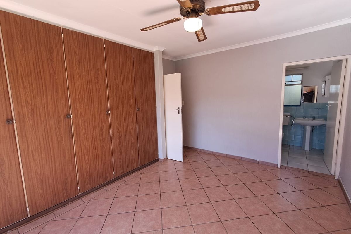 A bedroom featuring built-in wooden wardrobes, tiled flooring, a ceiling fan, and an en-suite bathroom.