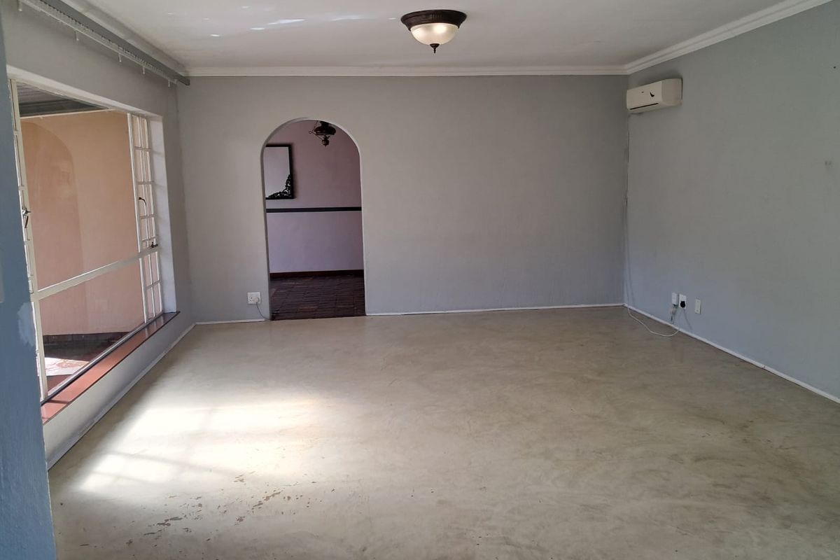 A spacious, empty living room featuring polished concrete floors, an arched doorway, and a wall-mounted air conditioning unit.