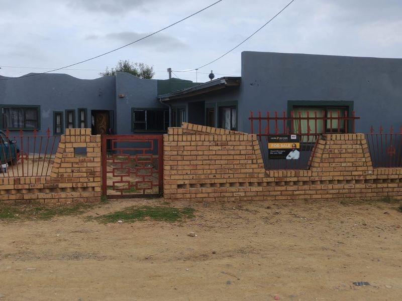 Front elevation of a single-story house featuring a brick boundary wall, metal security fencing, and a painted exterior finish.