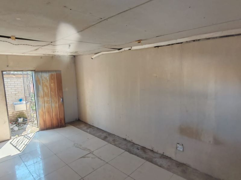 An empty living area featuring tiled flooring and a metal security door, requiring significant renovation to address ceiling and wall finish defects.