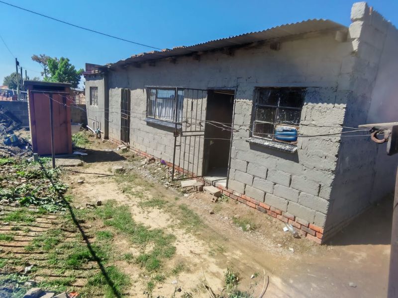 Rear view of a single-story house featuring unplastered concrete block walls, metal security gates, and a corrugated metal roof in need of exterior maintenance.