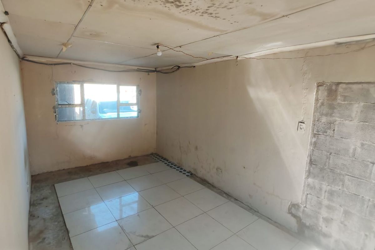 An empty bedroom requiring significant renovation, featuring tiled flooring, exposed electrical wiring, and visible water damage on the ceiling.