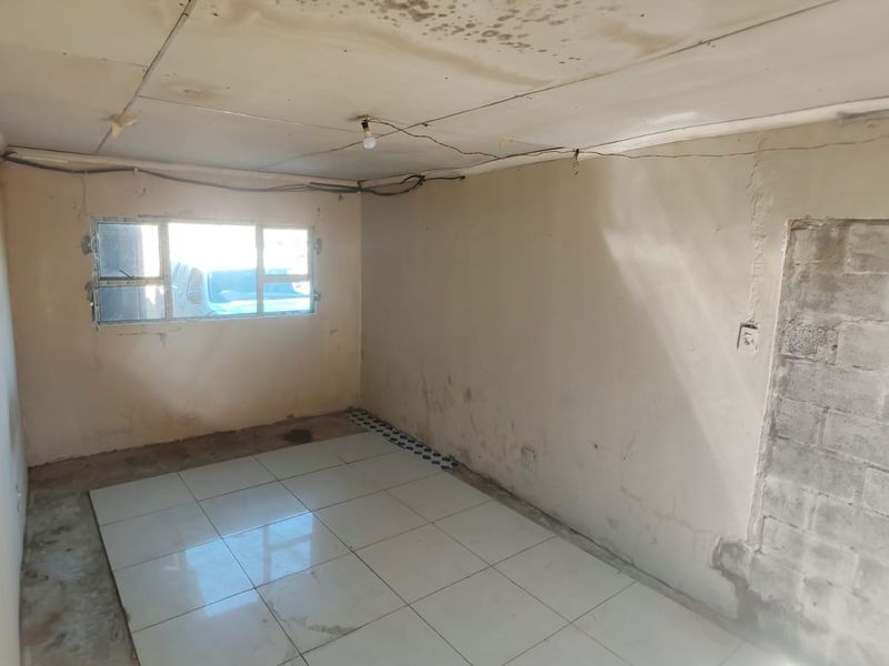 An empty bedroom requiring significant renovation, featuring tiled flooring, exposed electrical wiring, and visible water damage on the ceiling.