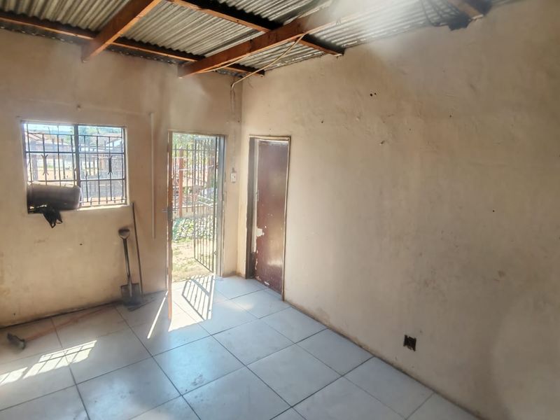 An empty, basic living area featuring tiled floors, exposed roof structure, and security fixtures on the door and window.