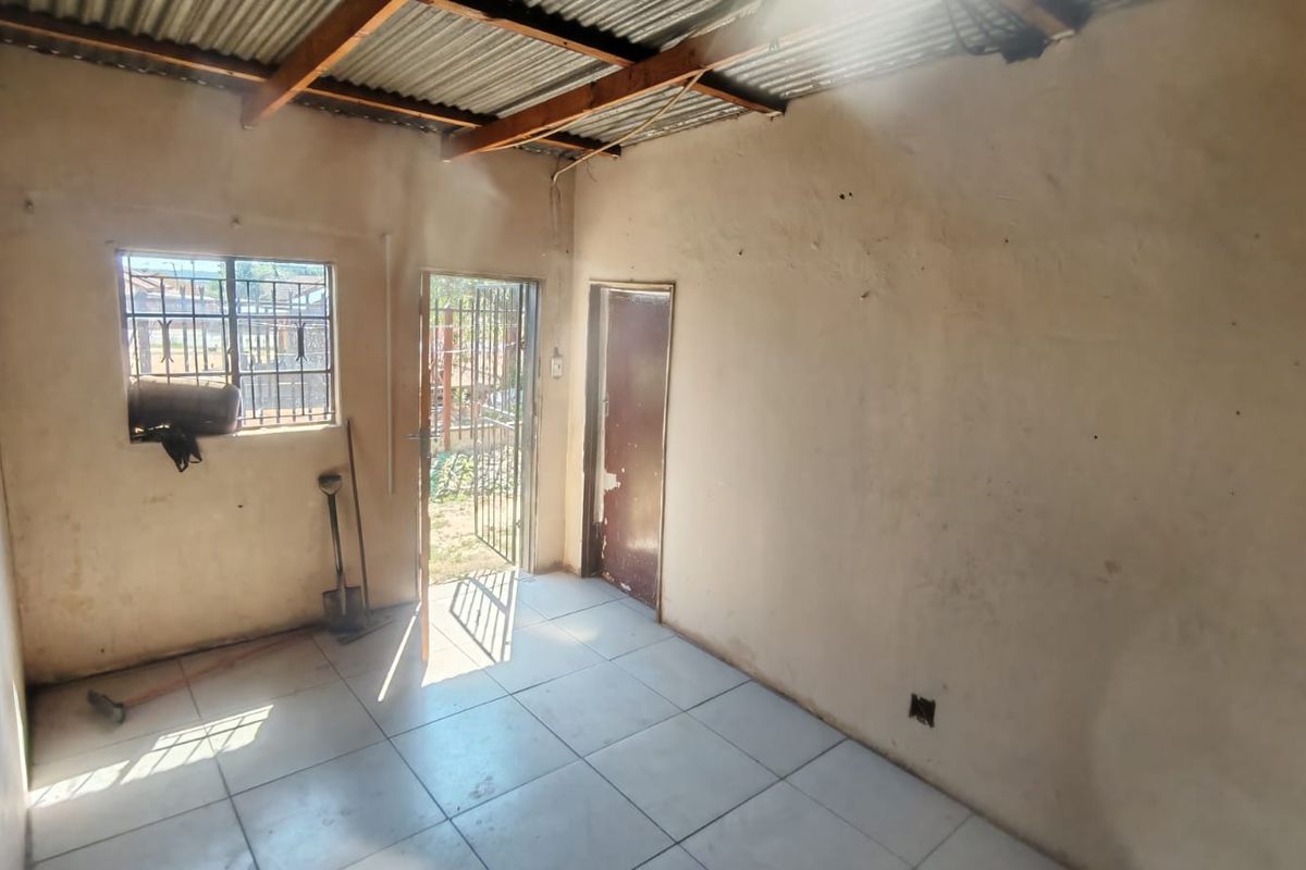 An empty, basic living area featuring tiled floors, exposed roof structure, and security fixtures on the door and window.