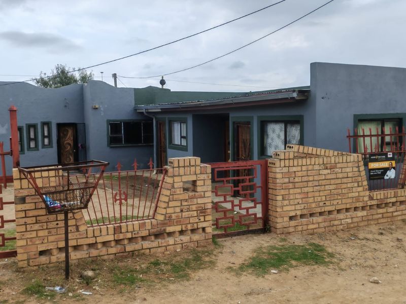 Front elevation of a single-story house featuring a painted facade, aluminium windows, and a brick boundary wall with metal security fencing.