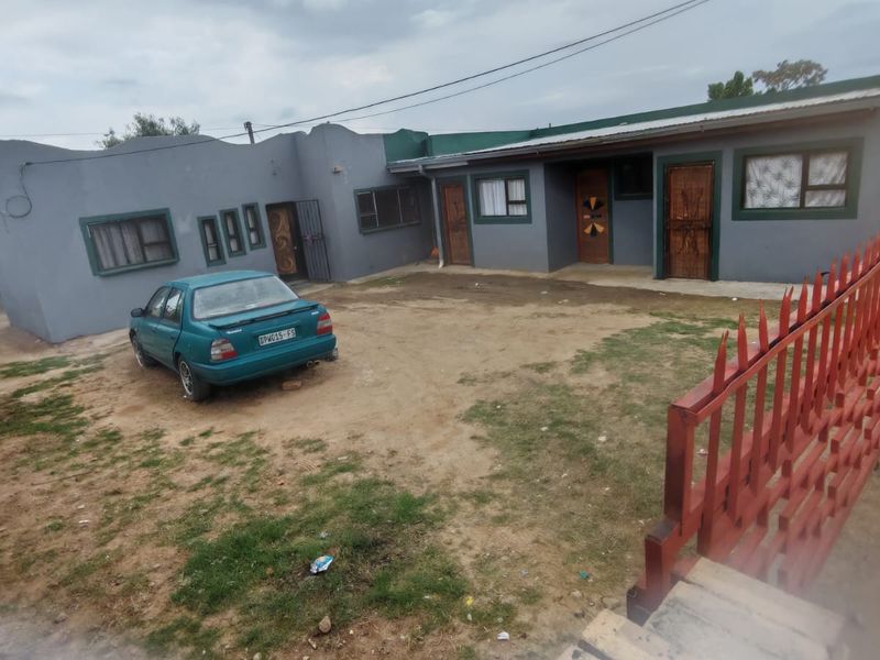 Front view of a single-story residential property featuring a large open yard area, metal security gates, and multiple access points.