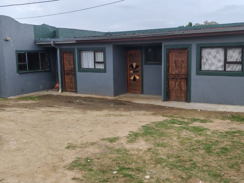 Front elevation of a single-story residential property featuring painted masonry walls, multiple entrance doors with security gates, and aluminium window frames.