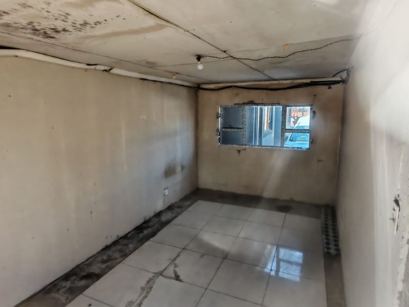 An empty bedroom requiring significant renovation, featuring tiled floors, an aluminium window, and visible ceiling and wall deterioration.