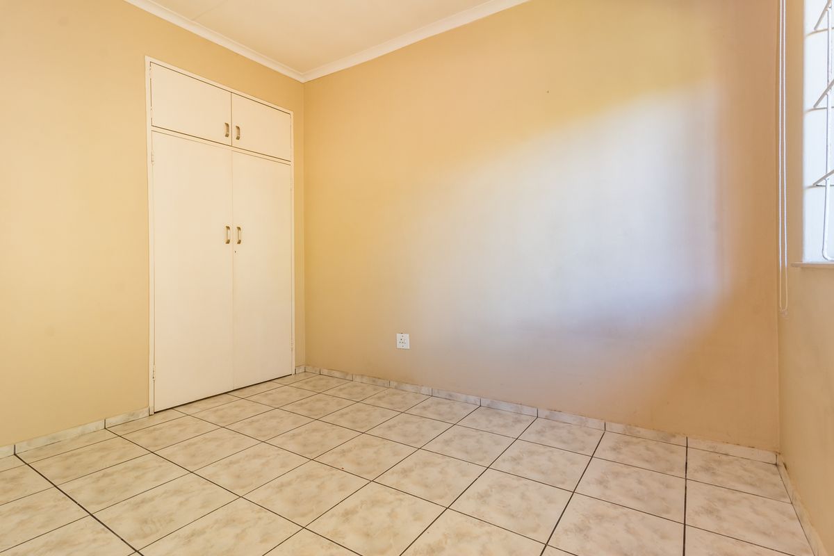 An empty bedroom featuring neutral wall paint, tiled flooring, and built-in storage cupboards.