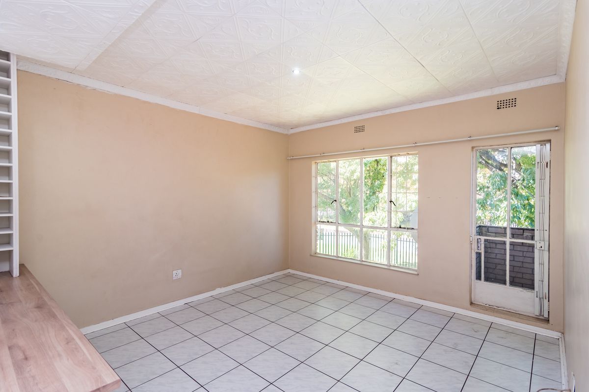 An empty living room featuring tiled flooring, textured ceiling tiles, built-in shelving, and direct access to an outdoor area through a glass panel door.