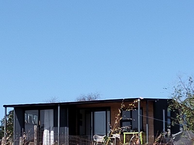A modern modular-style home featuring dark corrugated metal cladding, timber accents, and large sliding glass doors opening onto a covered patio area.