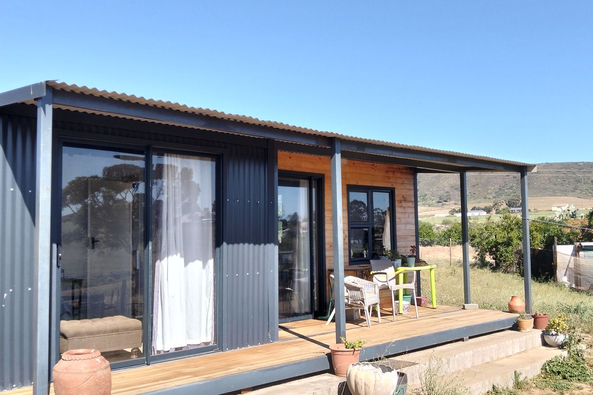A modern modular-style dwelling featuring a timber deck, corrugated metal exterior cladding, and large sliding glass doors opening to the outdoors.