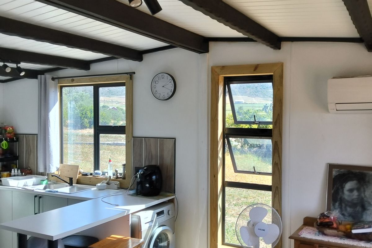 Compact kitchen area featuring exposed timber ceiling beams, track lighting, timber-framed windows, and integrated laundry facilities with a modern, functional layout.