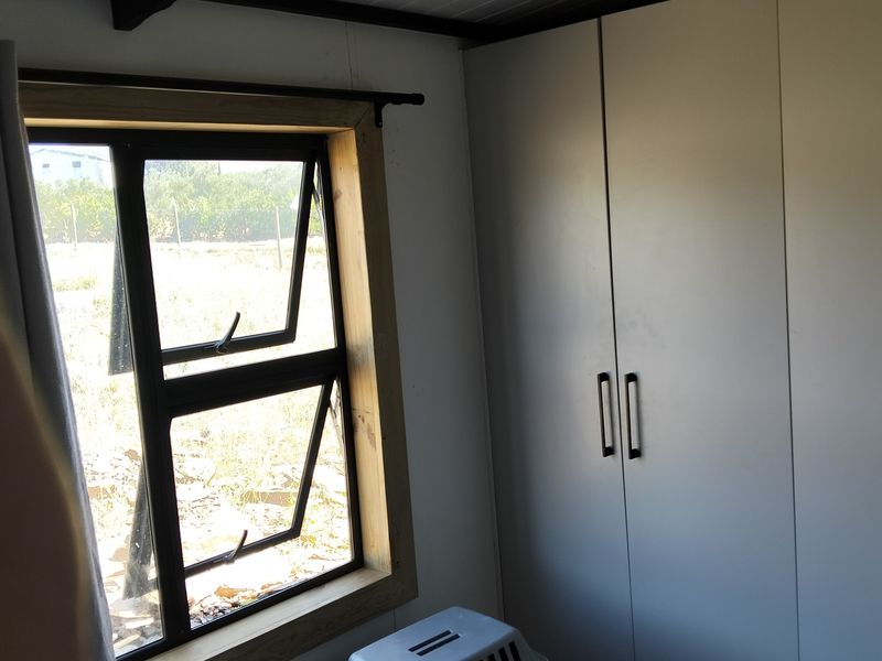 A bedroom featuring built-in cupboards, exposed ceiling beams, and a timber-framed window overlooking the exterior.