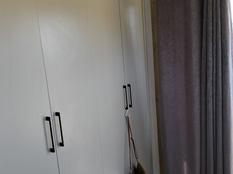 A bedroom interior featuring white built-in cupboards with modern black handles and a curtained window area.