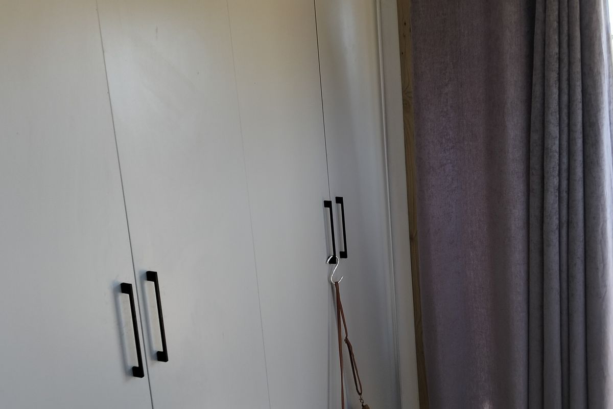 A bedroom interior featuring white built-in cupboards with modern black handles and a curtained window area.