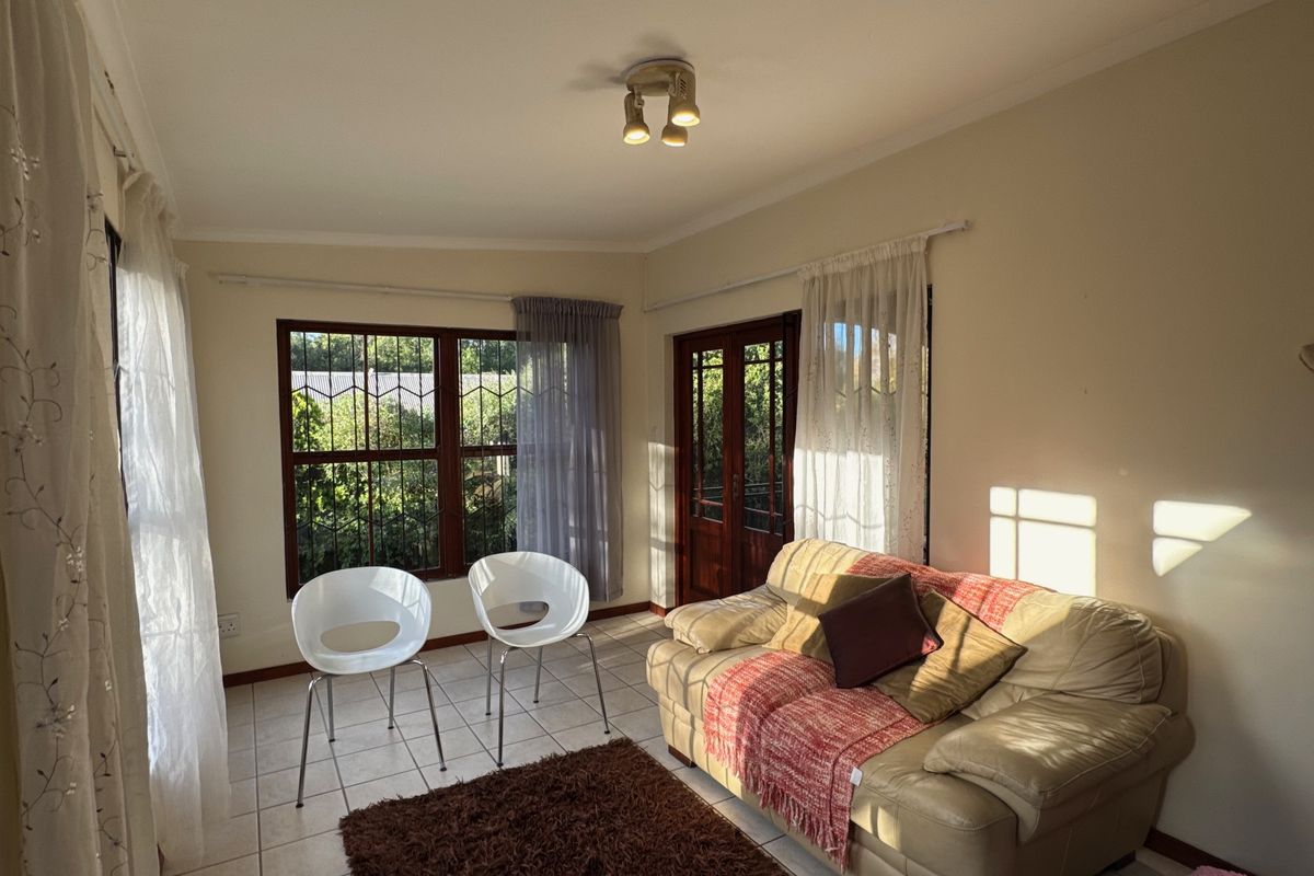 A sunlit living room featuring tiled flooring, security-barred windows, and a timber-framed glass door providing access to the exterior.