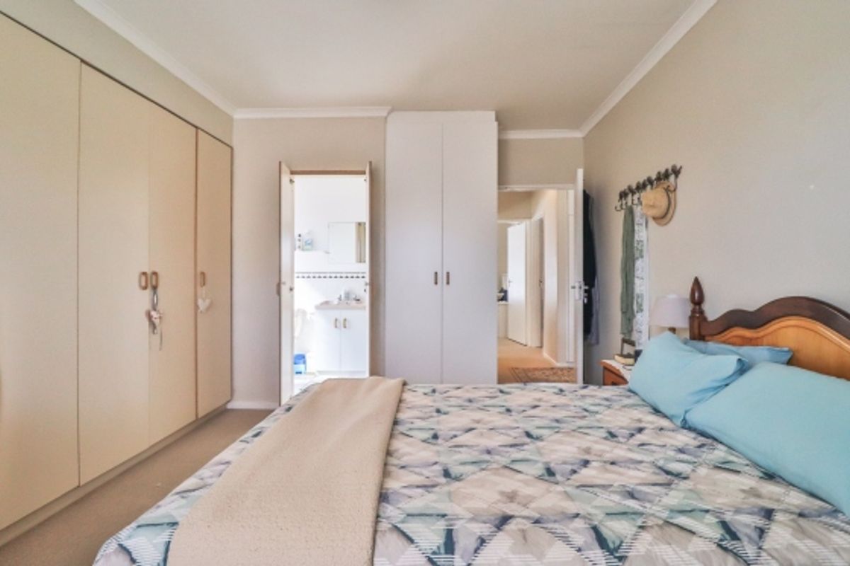 A well-proportioned bedroom featuring extensive built-in cupboard storage, neutral wall finishes, and direct access to an en-suite bathroom.