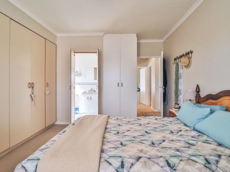 A well-proportioned bedroom featuring extensive built-in cupboard storage, neutral wall finishes, and direct access to an en-suite bathroom.