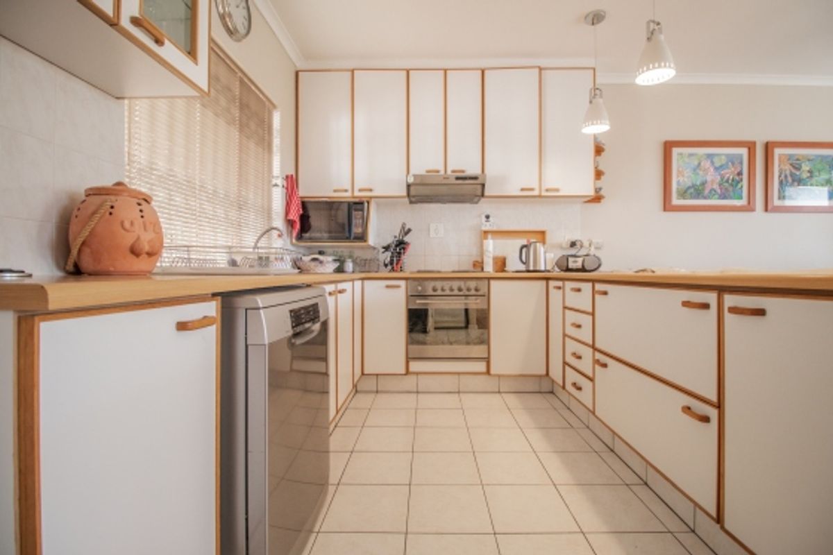 A functional U-shaped kitchen featuring white cabinetry with wood trim, laminate countertops, tiled flooring, and integrated stainless steel appliances.