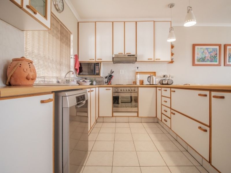 A functional U-shaped kitchen featuring white cabinetry with wood trim, laminate countertops, tiled flooring, and integrated stainless steel appliances.