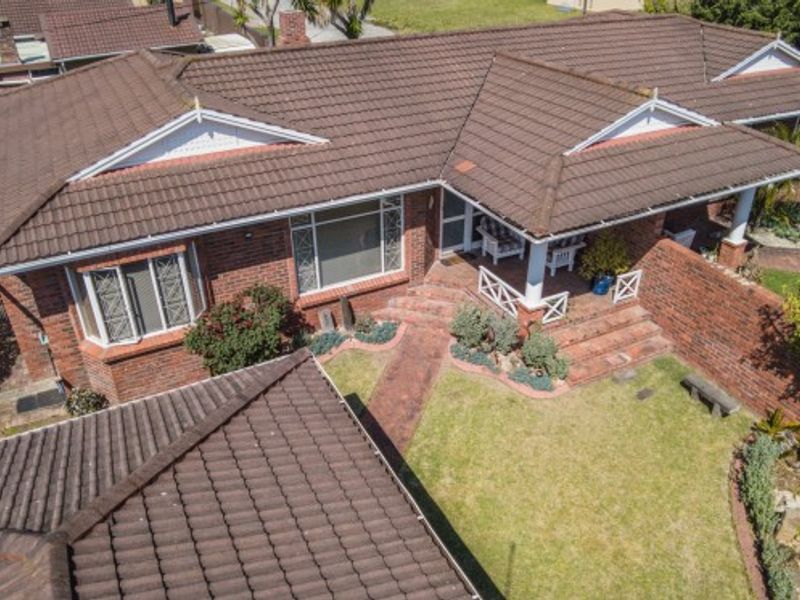 Aerial view of a brick townhouse featuring a tiled roof, covered patio area, and landscaped garden with a brick pathway.