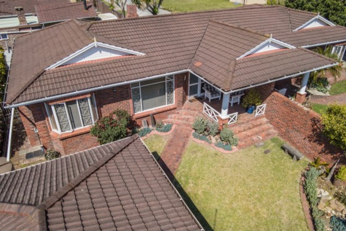 Aerial view of a brick townhouse featuring a tiled roof, covered patio area, and landscaped garden with a brick pathway.