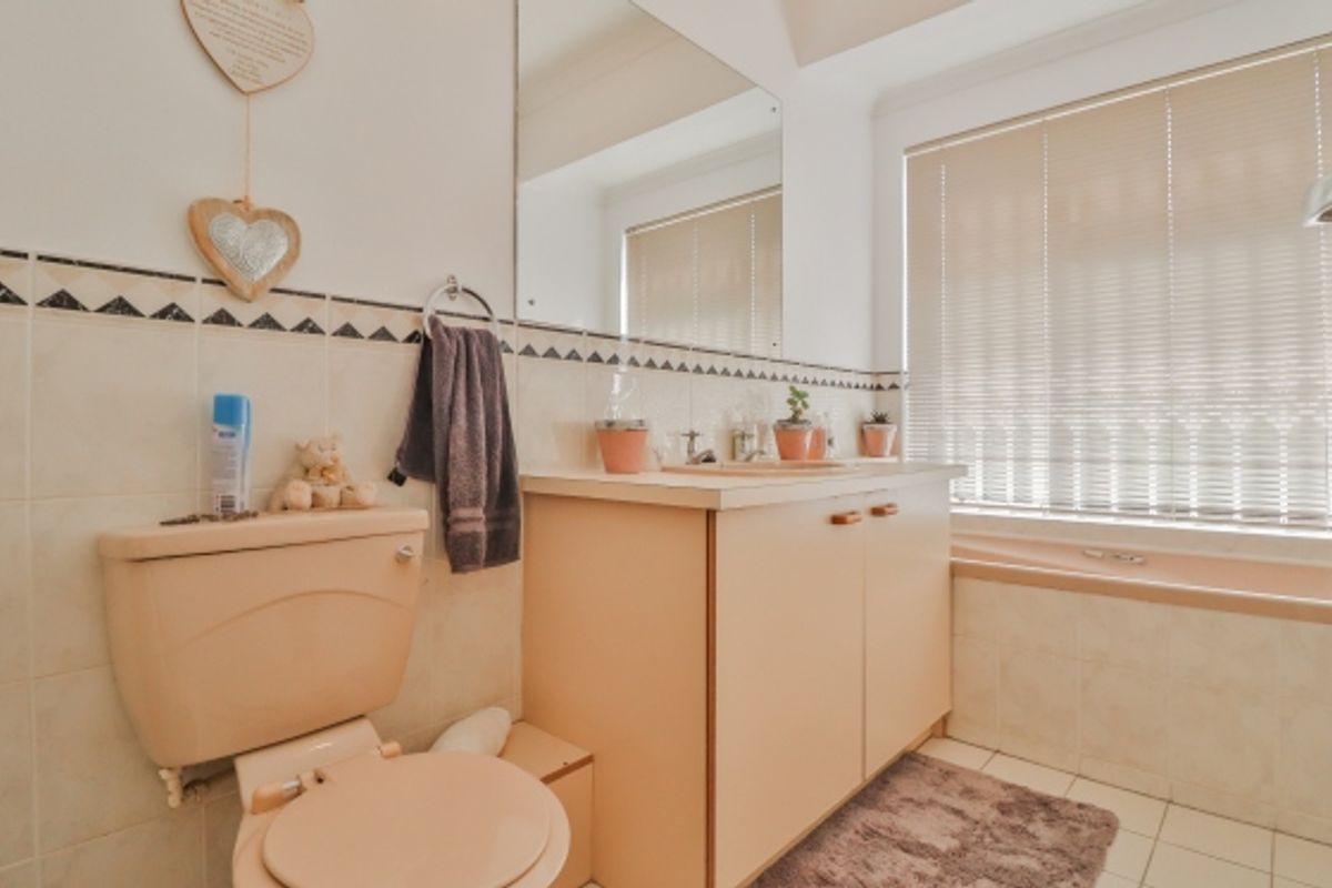 A functional bathroom featuring a vanity cabinet, integrated sink, toilet, and bathtub with neutral wall tiling and venetian blinds.