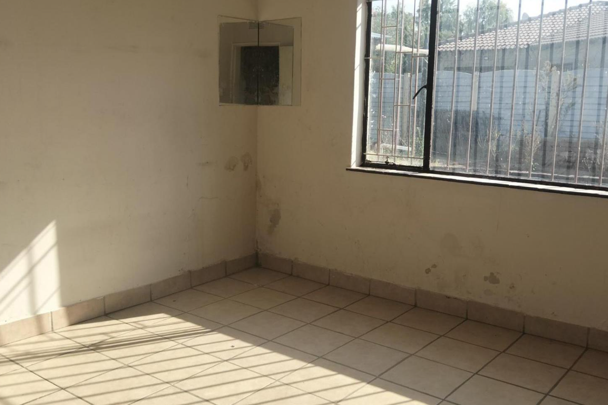 An empty bedroom featuring tiled flooring, security bars on the window, and wall surfaces requiring maintenance and repainting.