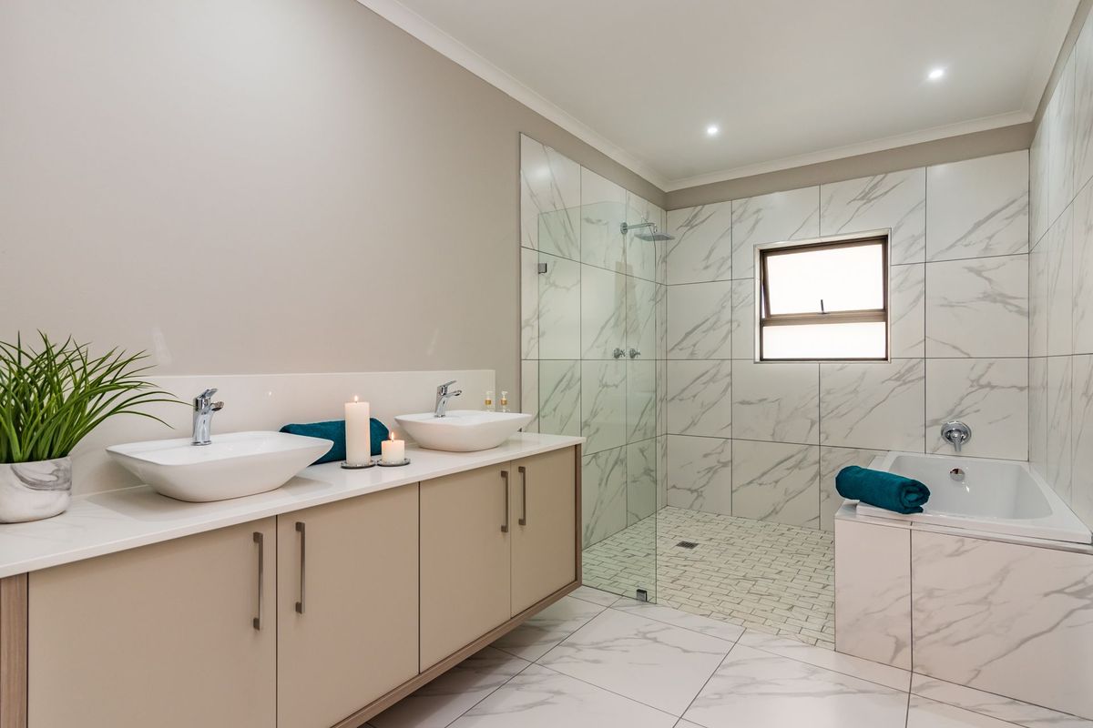 Modern bathroom featuring a double vanity with vessel sinks, a spacious walk-in shower with glass screen, and a built-in bathtub with marble-look tiling.