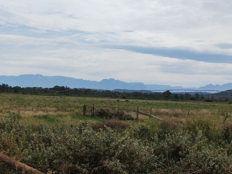 Expansive farm landscape featuring a large irrigation pivot system, wire fencing, and scenic mountain views in the background.