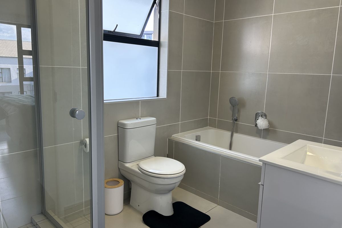 A modern bathroom featuring a built-in bathtub, separate shower enclosure, vanity basin, and neutral wall tiling with a top-hung window for ventilation.