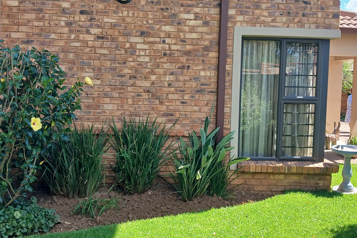 A well-maintained rear exterior view of the townhouse featuring face brick walls, aluminium window frames with security bars, and a paved patio area.