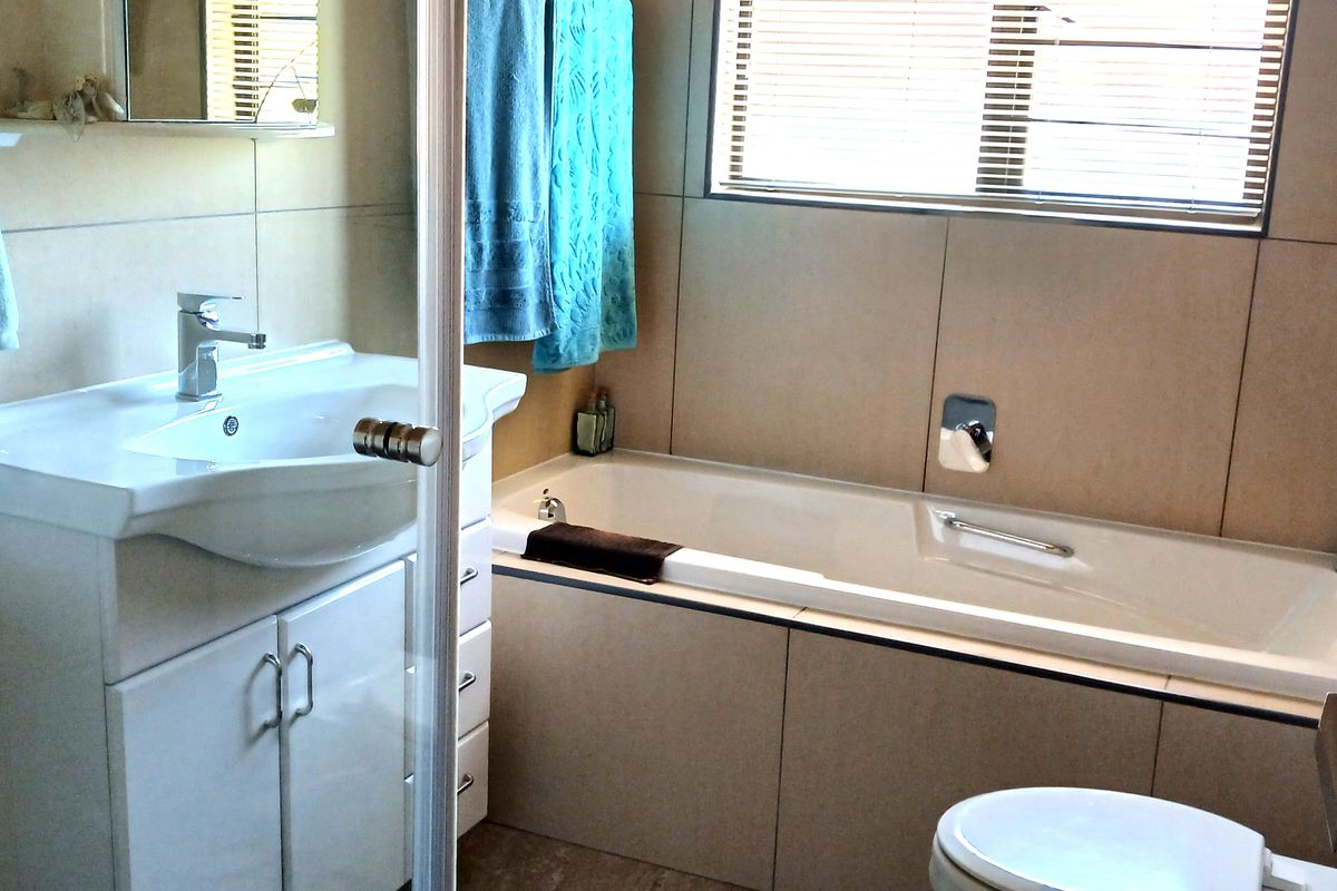 A functional bathroom featuring a vanity with basin, built-in bathtub, wall-mounted toilet, and neutral wall tiling.