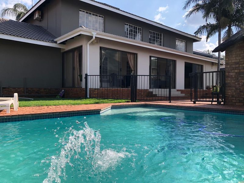 Rear view of the property featuring a swimming pool, brick paved surround, metal safety fencing, and direct access to the home via sliding glass doors.