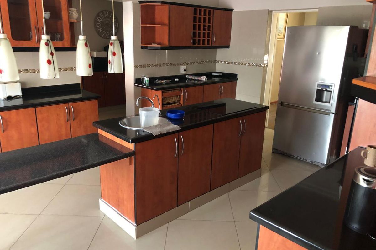 A functional kitchen featuring wooden cabinetry, dark granite countertops, a central island with a sink, and tiled flooring.
