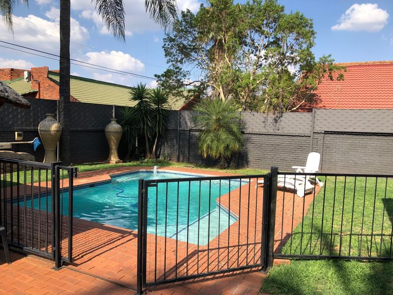 A private outdoor pool area featuring a paved surround, metal safety fencing, and a painted brick boundary wall in a landscaped garden setting.