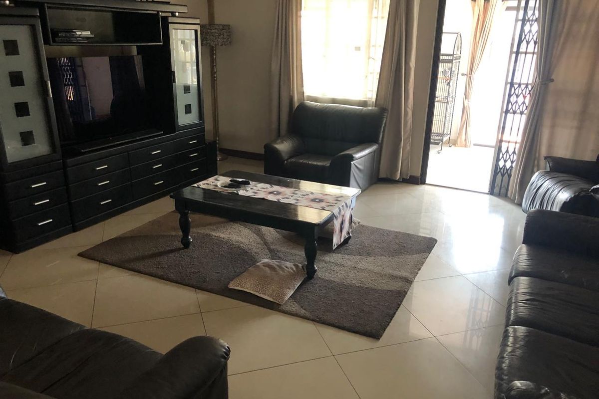 A spacious living room featuring large format floor tiles and direct access to an outdoor area through a security gate and sliding door.