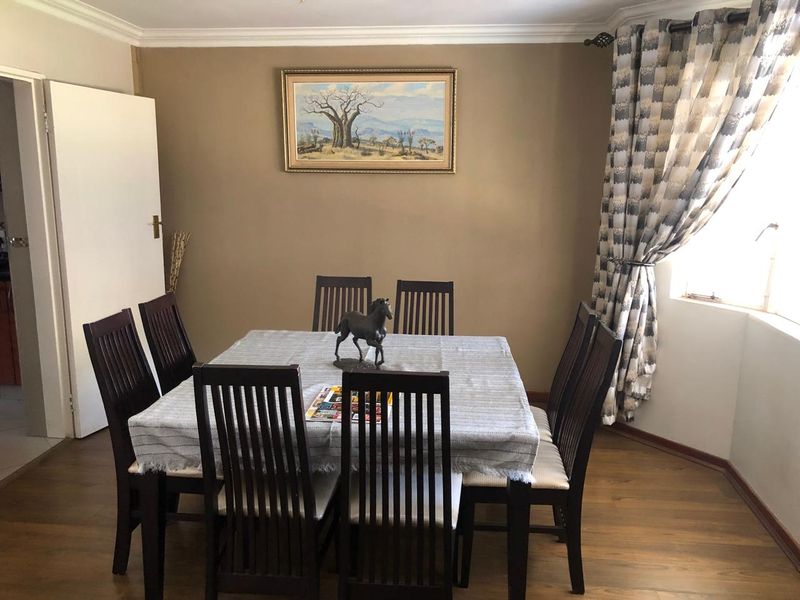A dining room featuring laminate flooring, neutral wall tones, and a window with curtains, providing a functional space for family meals.