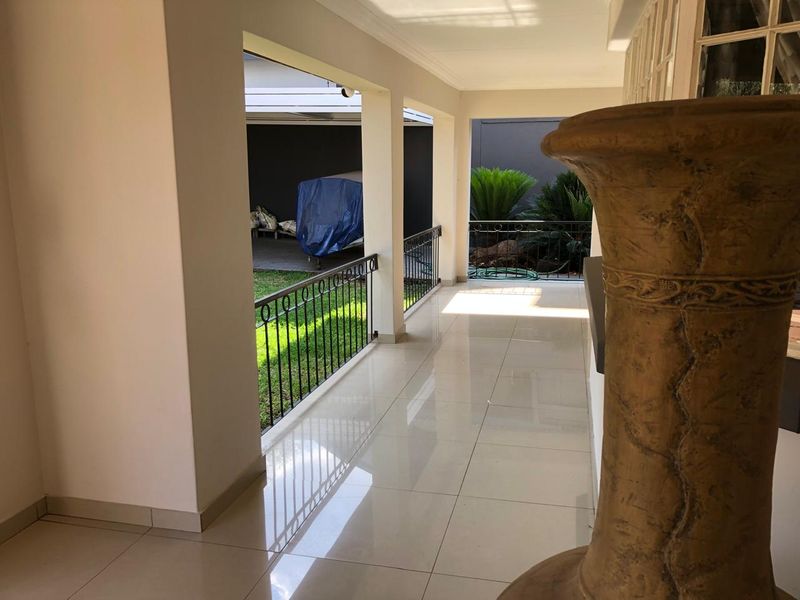 A spacious covered patio featuring polished floor tiles and a wrought iron balustrade, overlooking a neat garden area.