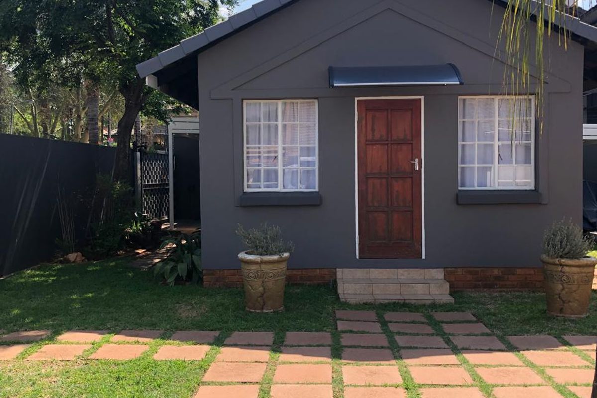 A well-maintained rear exterior view of a house featuring a dark grey facade, timber door, tiled roof, and a paved garden walkway.