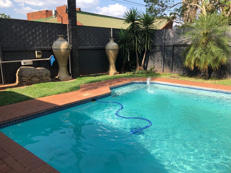 A well-maintained swimming pool area featuring brick coping, a water feature, and a secure perimeter boundary wall.