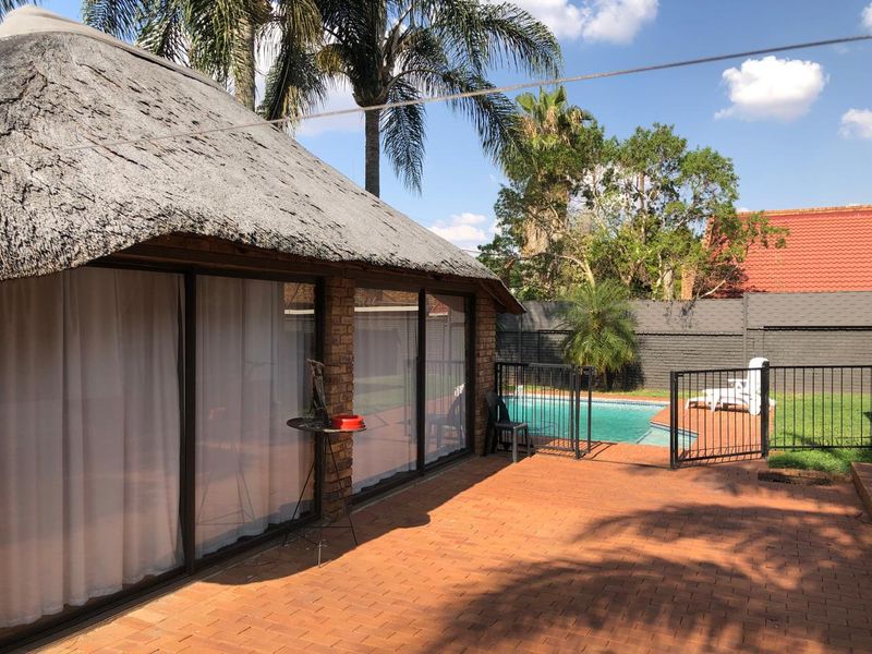 Outdoor entertainment area featuring a thatched-roof structure, paved patio, and a swimming pool enclosed by metal fencing.